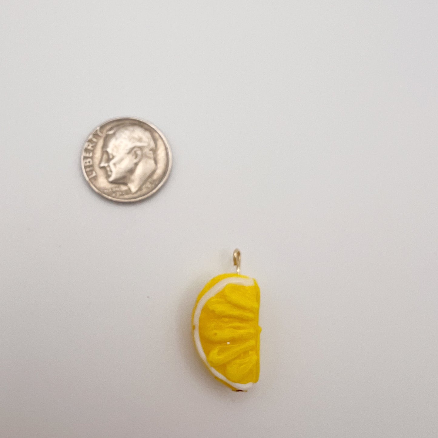 Yellow lemon slice charm next to a U.S. quarter on a light gray background