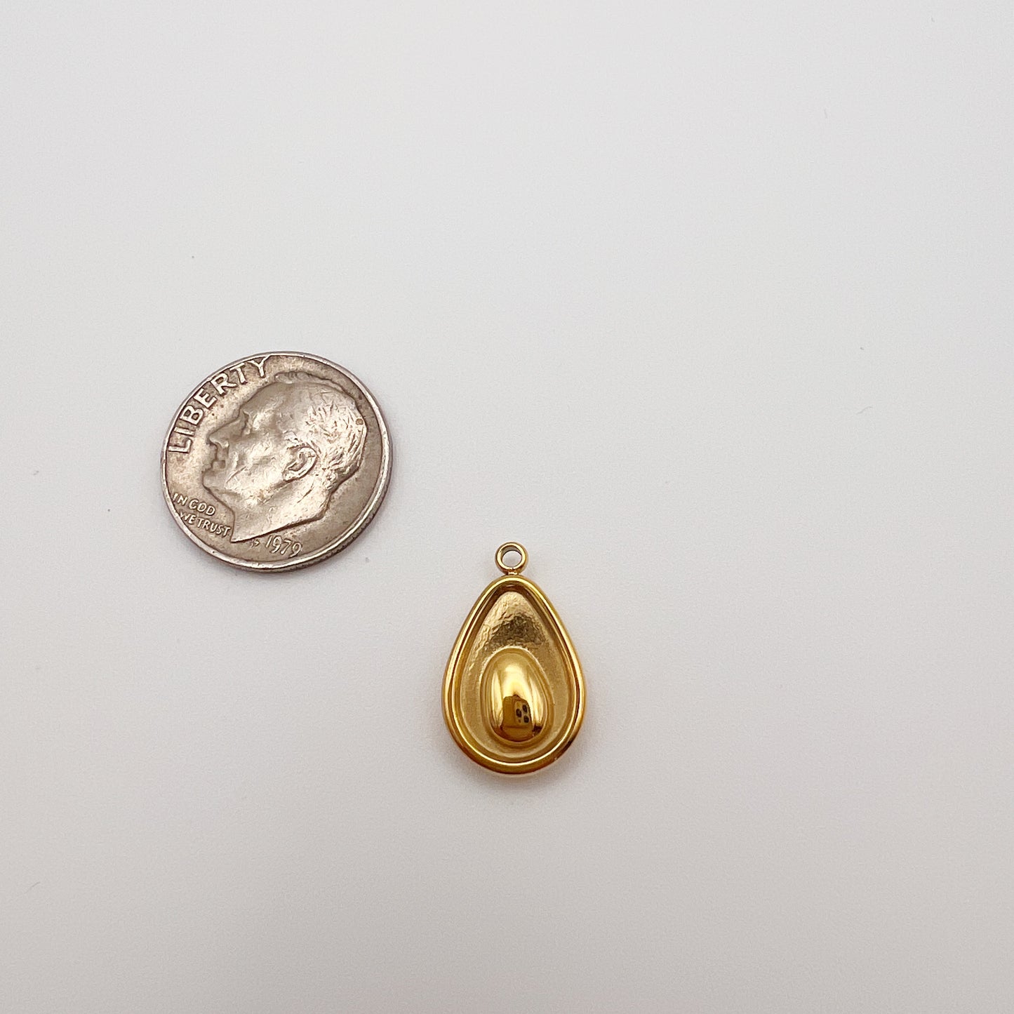 Gold teardrop pendant next to a quarter on a white background