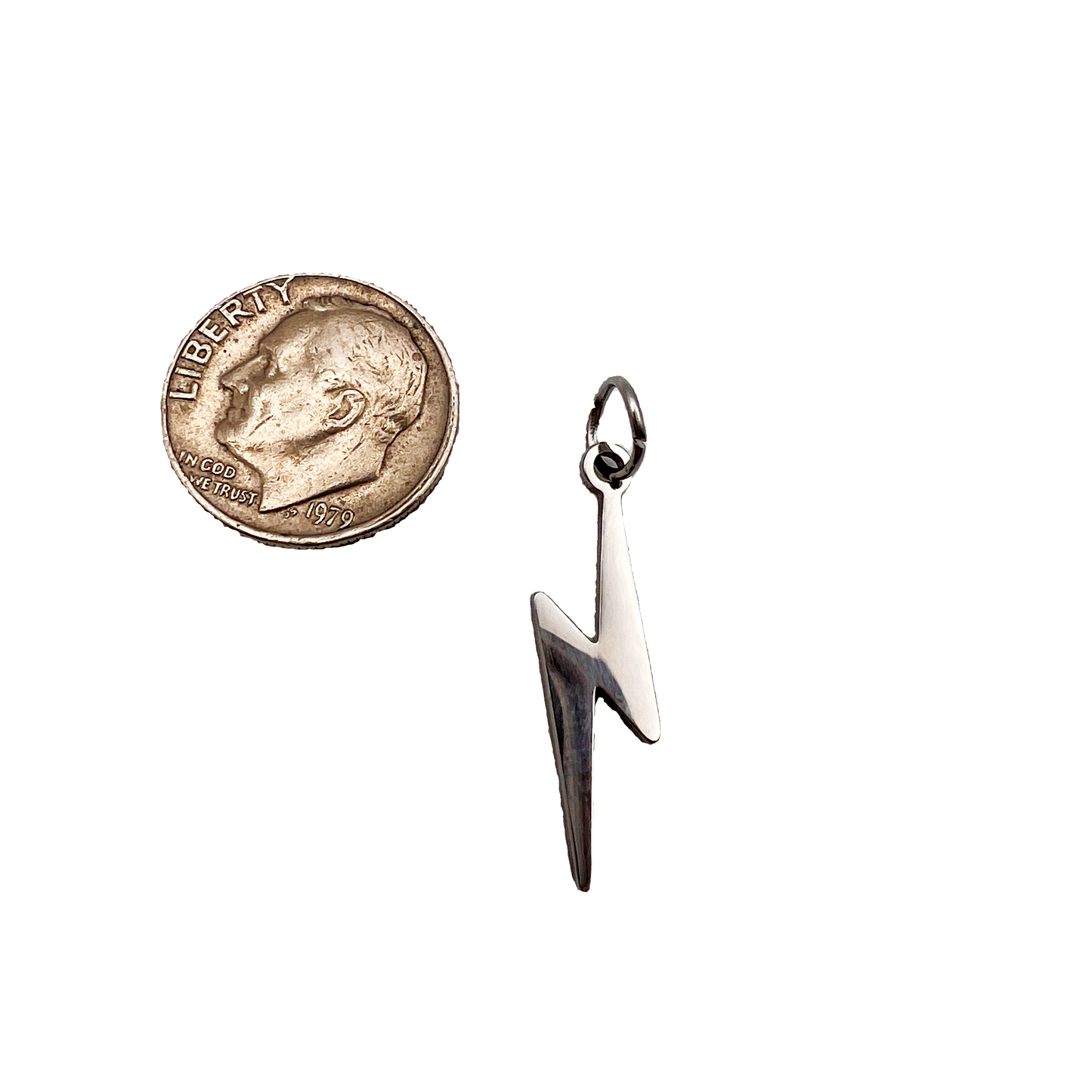 Silver lightning bolt pendant next to a coin on a light gray background