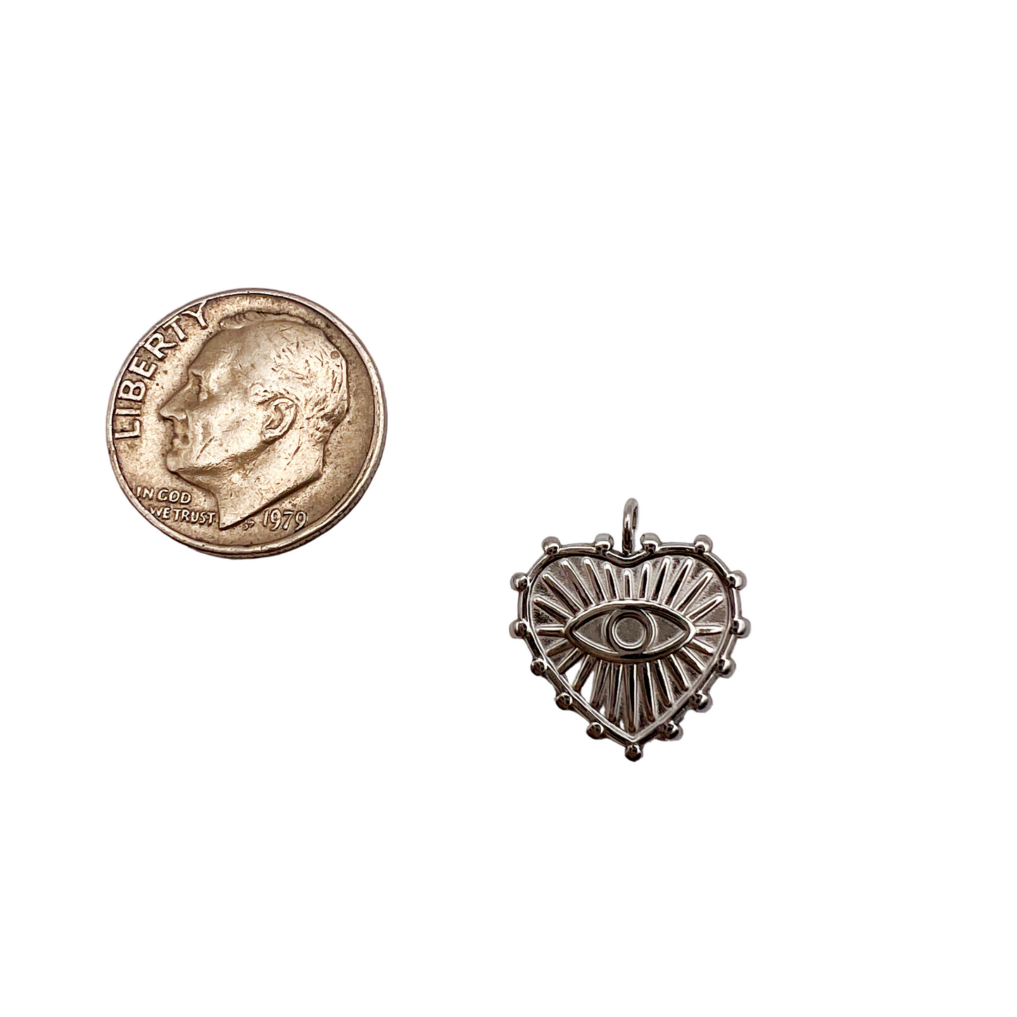 Small silver decorative item with eye design next to a U.S. quarter on a light gray background
