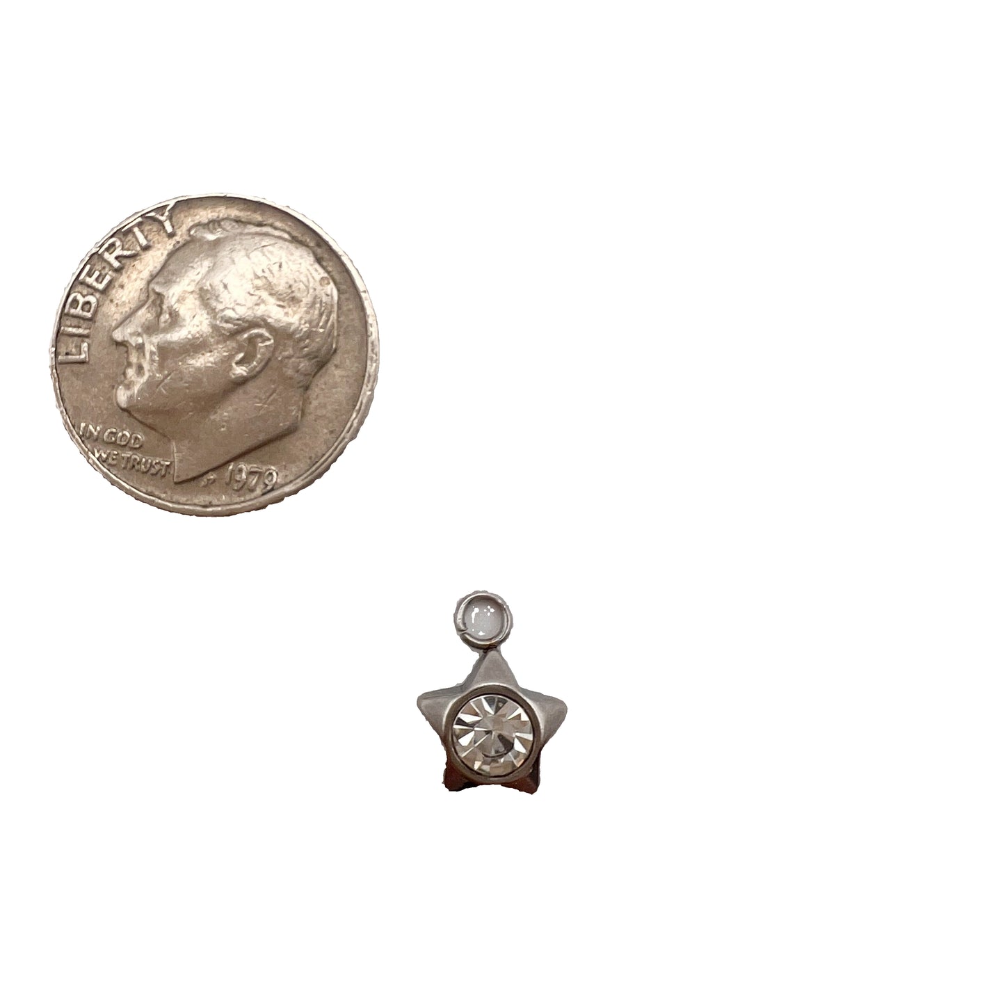Star-shaped charm with a clear gemstone next to a quarter on a white background