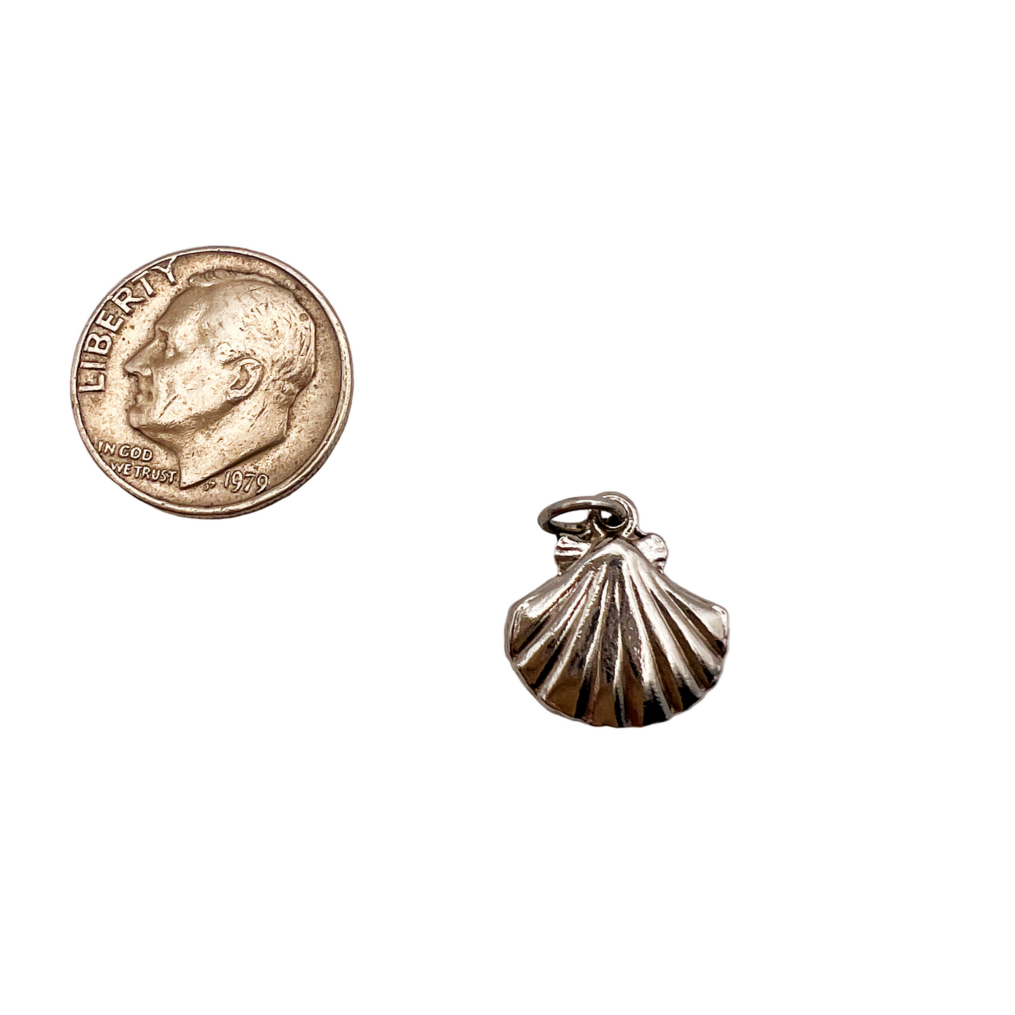Silver shell charm next to a coin on a light gray background