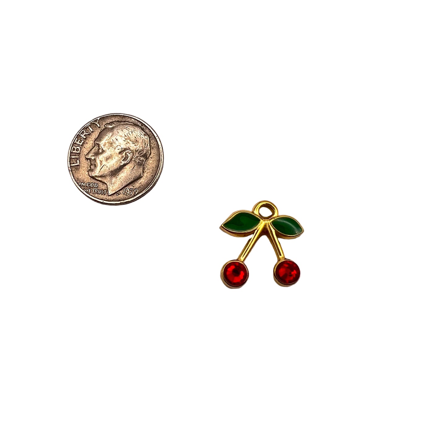 Small gold cherry pendant with red and green stones next to a quarter on a white background