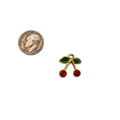 Small gold cherry pendant with red and green stones next to a quarter on a white background