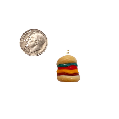 Miniature hamburger charm next to a quarter on a white background