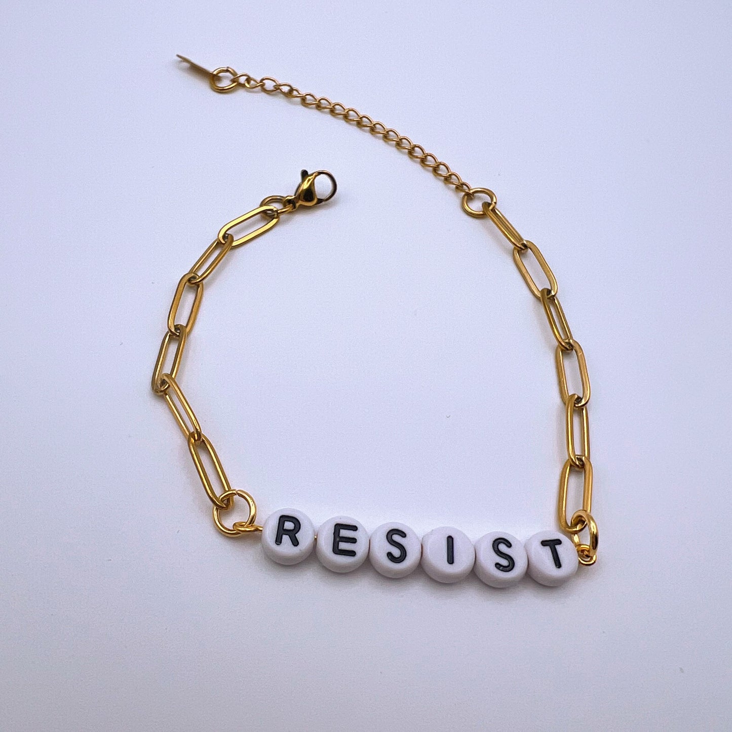 Gold chain bracelet with 'RESIST' beads on a white background