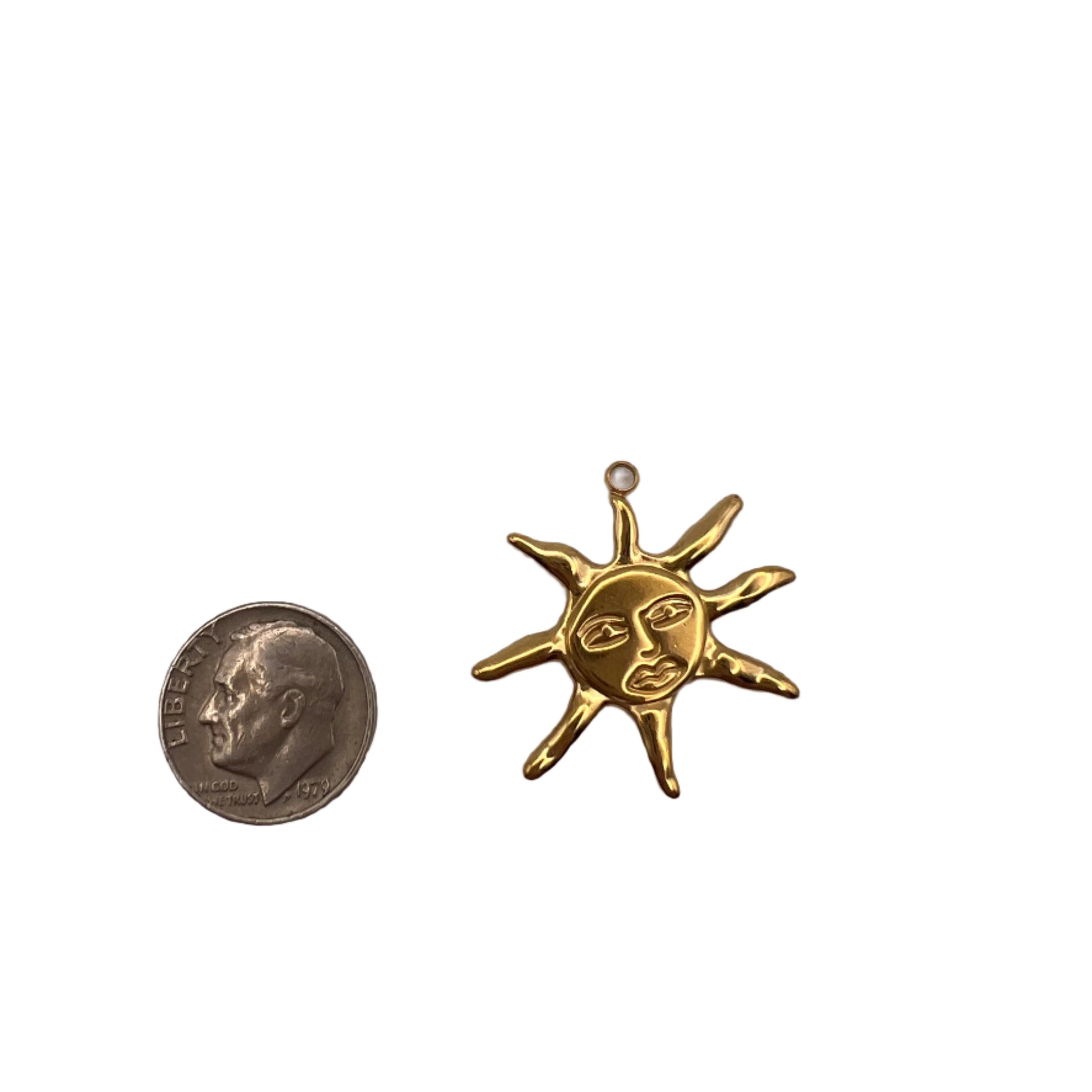 Gold sun-shaped pendant next to a quarter on a white background