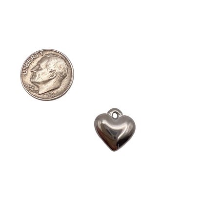 Silver heart-shaped charm next to a quarter on a light gray background