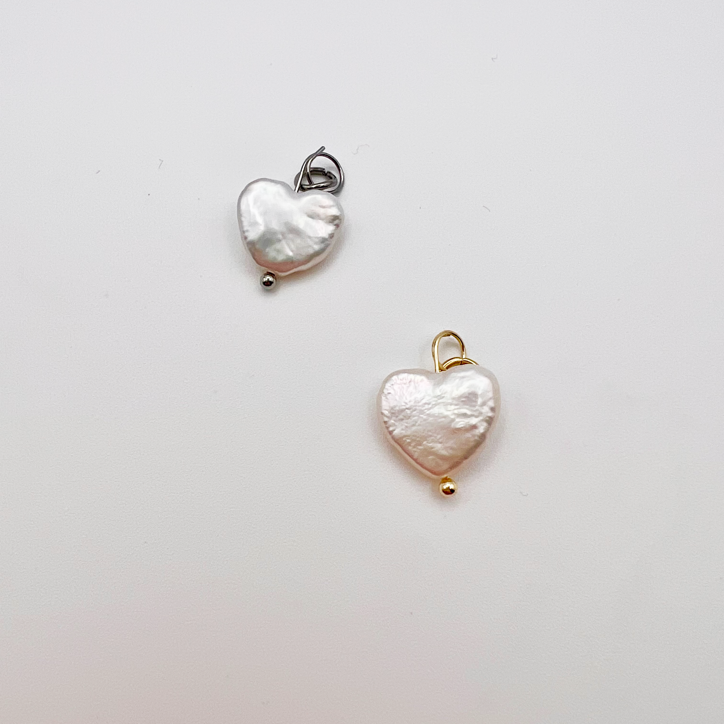Two heart-shaped pendants, one silver and one gold, on a light gray background.