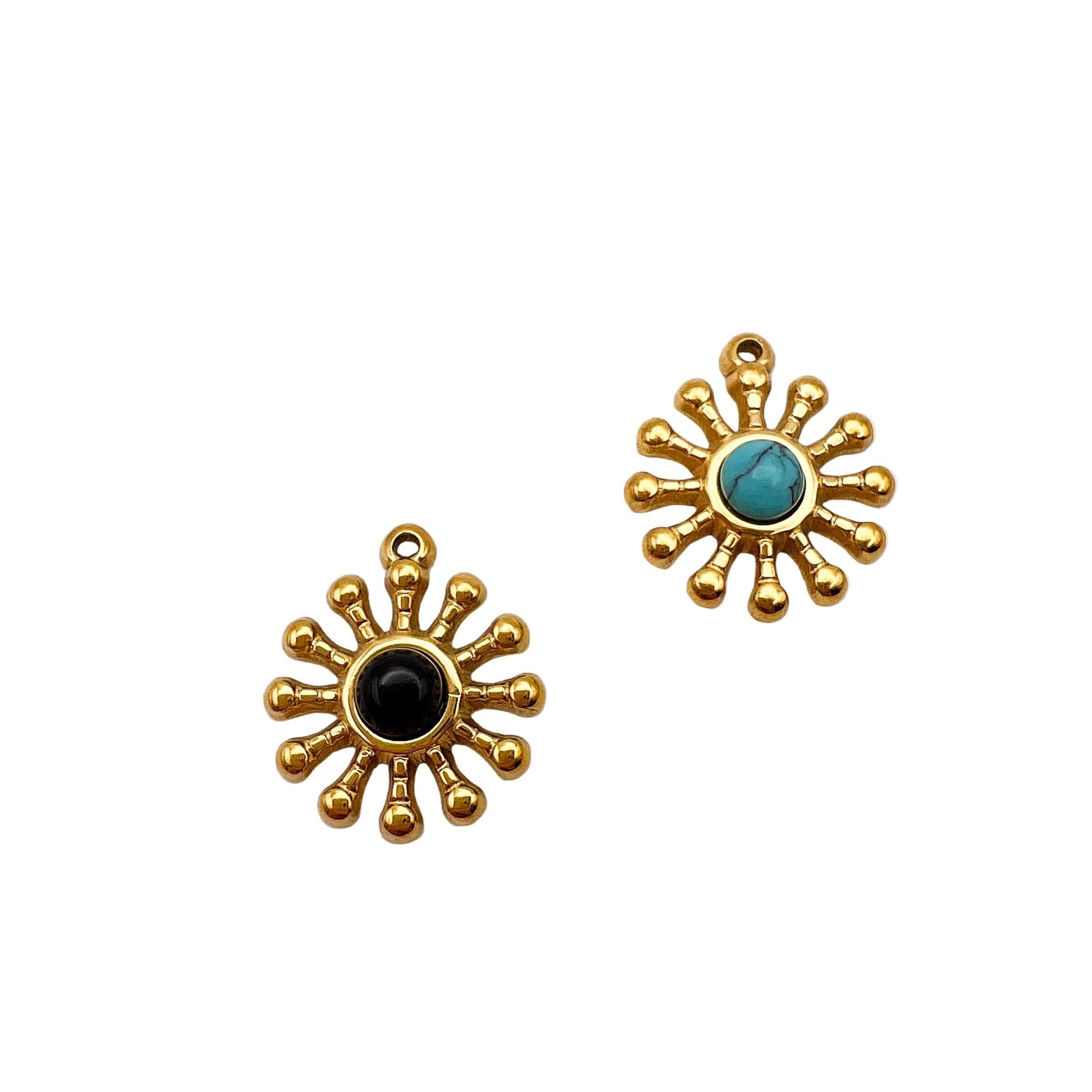 Two sun-shaped gold charms with central stones on a white background, one with a black stone and the other with a turquoise stone, next to a quarter for scale.