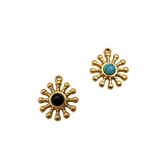 Two sun-shaped gold charms with central stones on a white background, one with a black stone and the other with a turquoise stone, next to a quarter for scale.