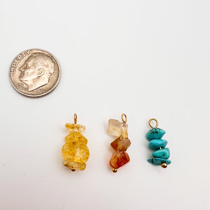 Three colorful stone pendants next to a quarter on a white background