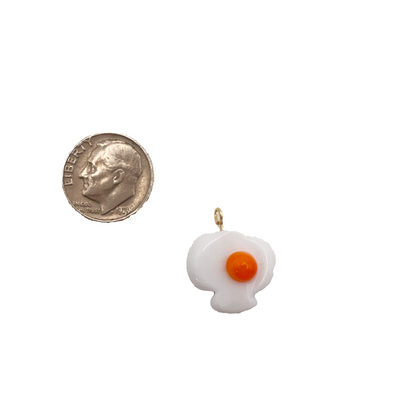 Small pendant shaped like a fried egg next to a quarter on a white background