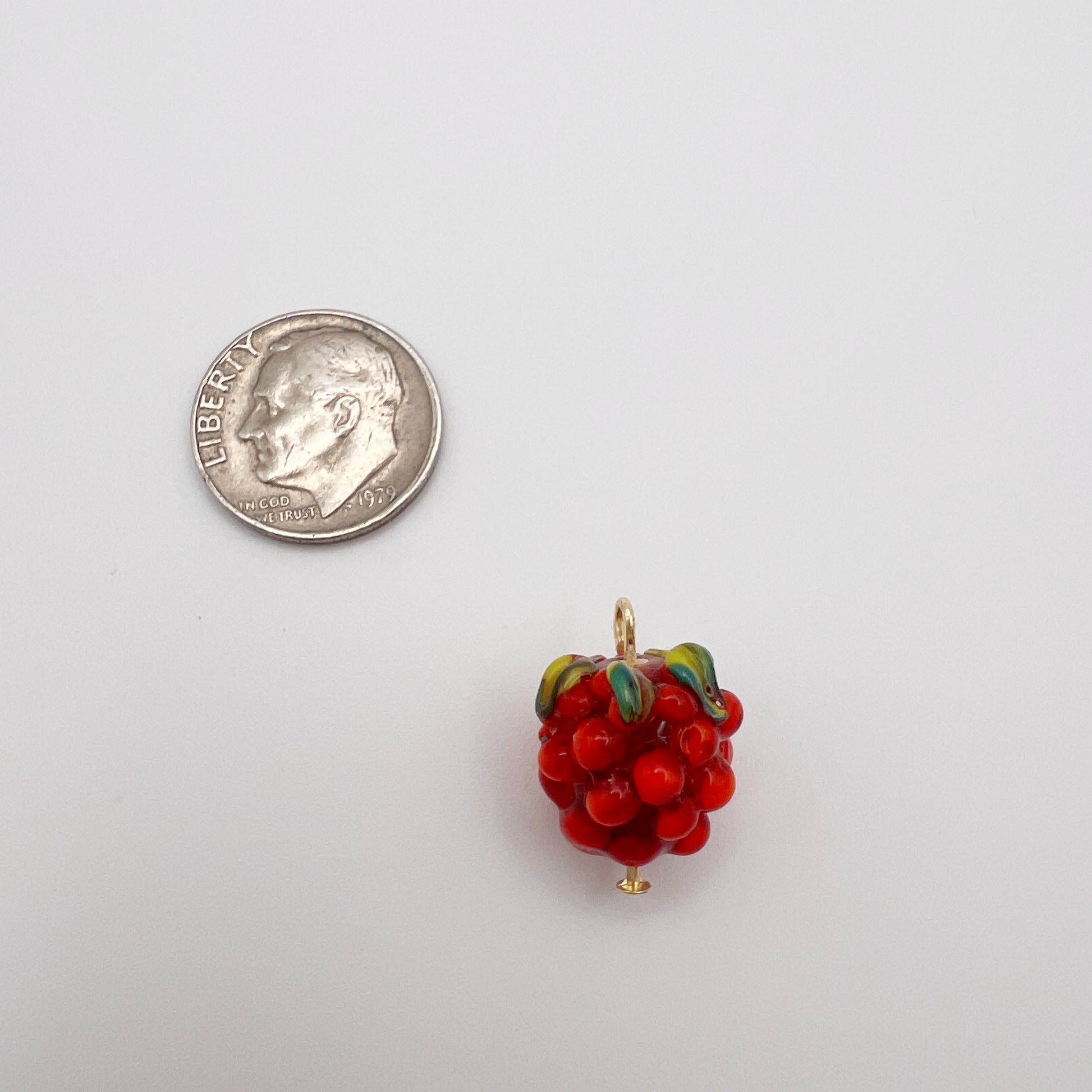 Red berry charm next to a quarter on a white background
