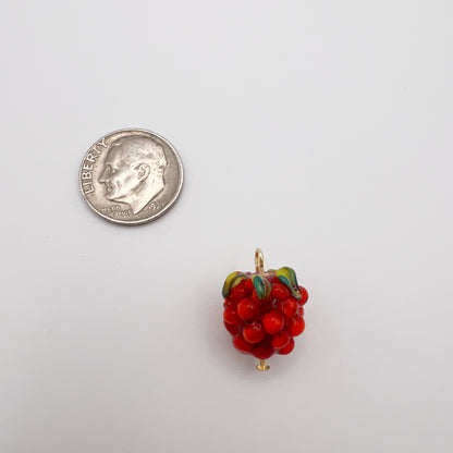 Red berry charm next to a quarter on a white background