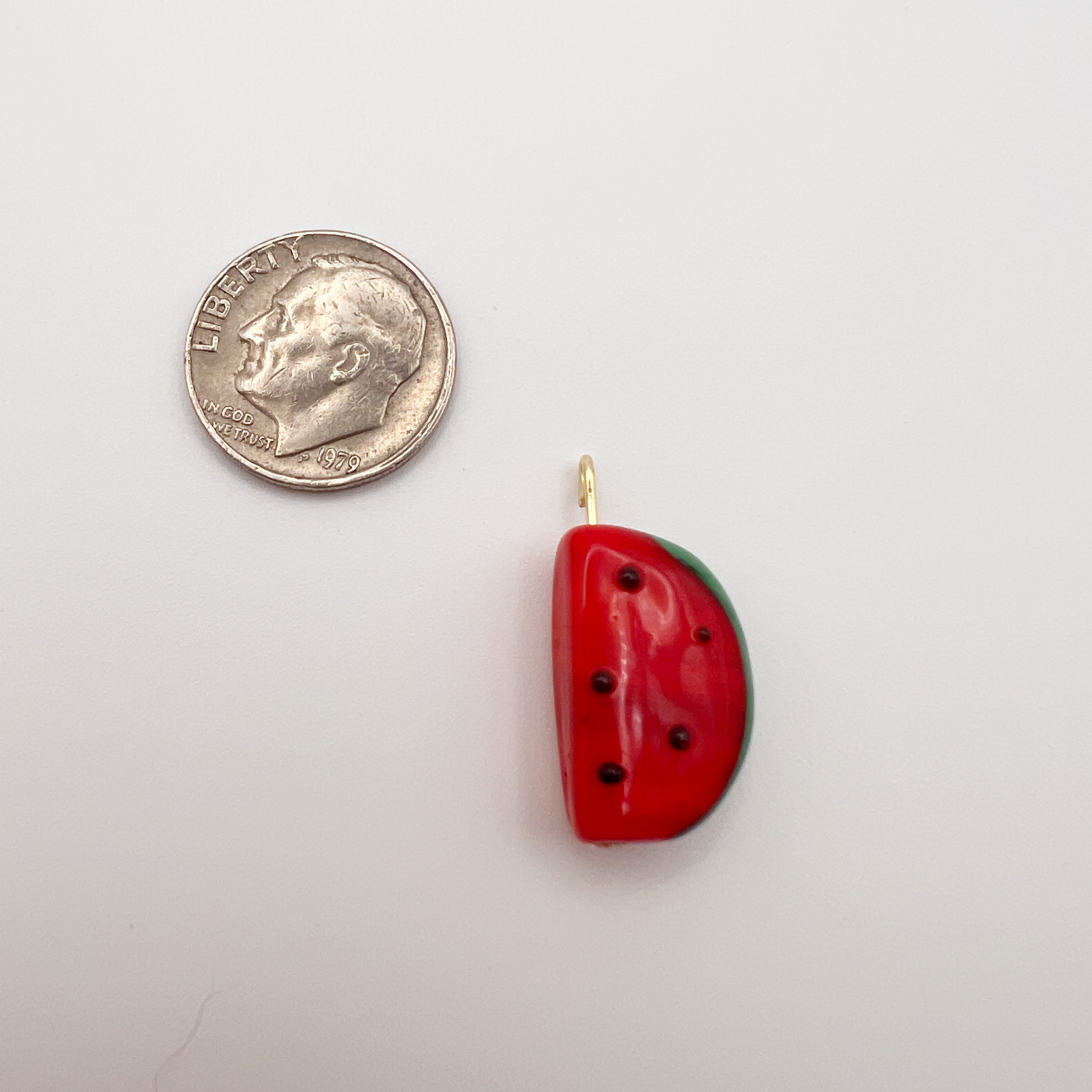 Watermelon slice pendant next to a quarter on a white background