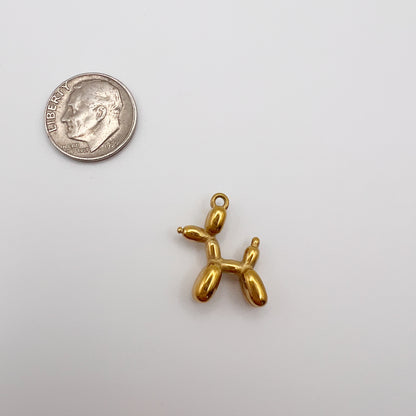 Gold balloon dog charm next to a quarter on a white background