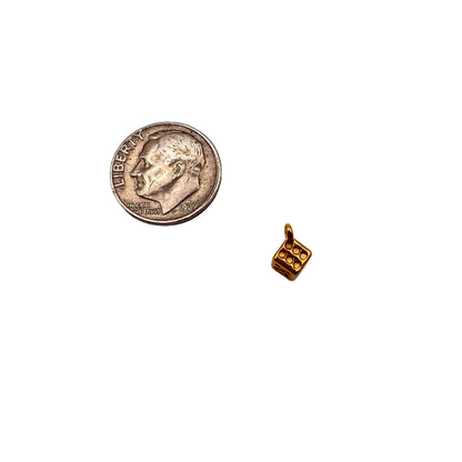 Small gold cube charm next to a U.S. quarter on a white background