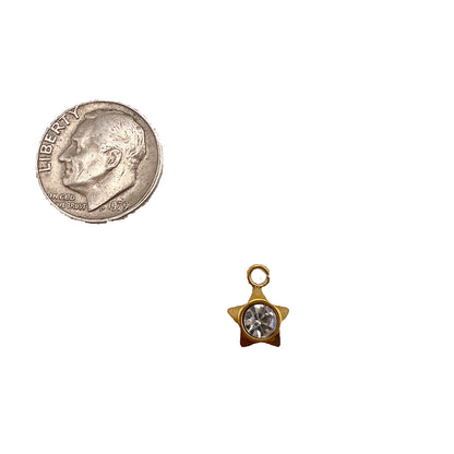 Gold star-shaped charm with a clear gemstone next to a quarter on a white background