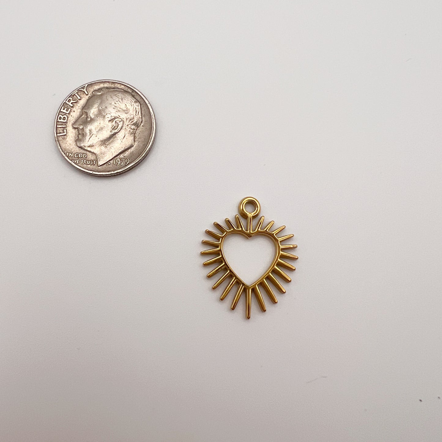 Gold heart-shaped pendant with sunburst design next to a quarter on a white background