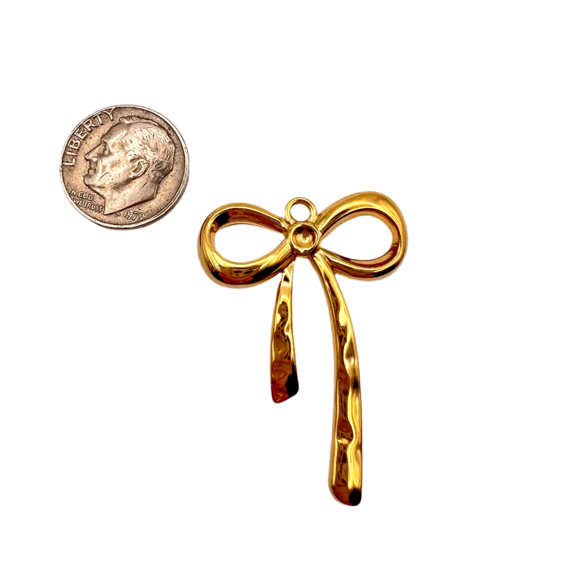 Gold bow-shaped pendant next to a quarter for scale on a white background