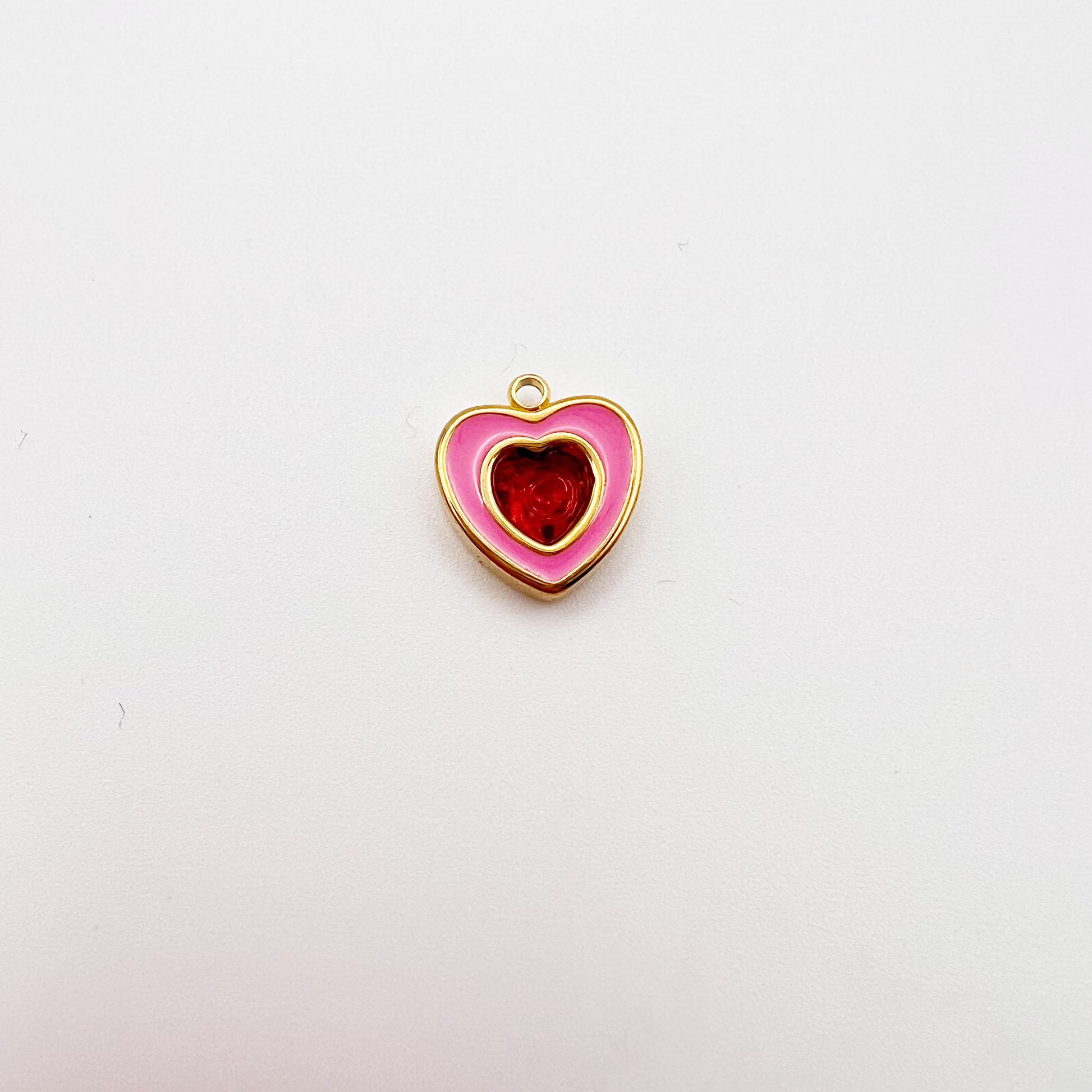 Heart-shaped pendant with pink border and red center on a white background