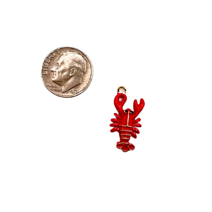 Red lobster charm next to a quarter on a white background