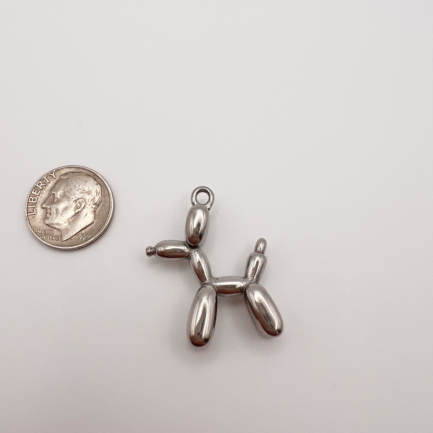 Metallic balloon dog charm next to a quarter on a white background