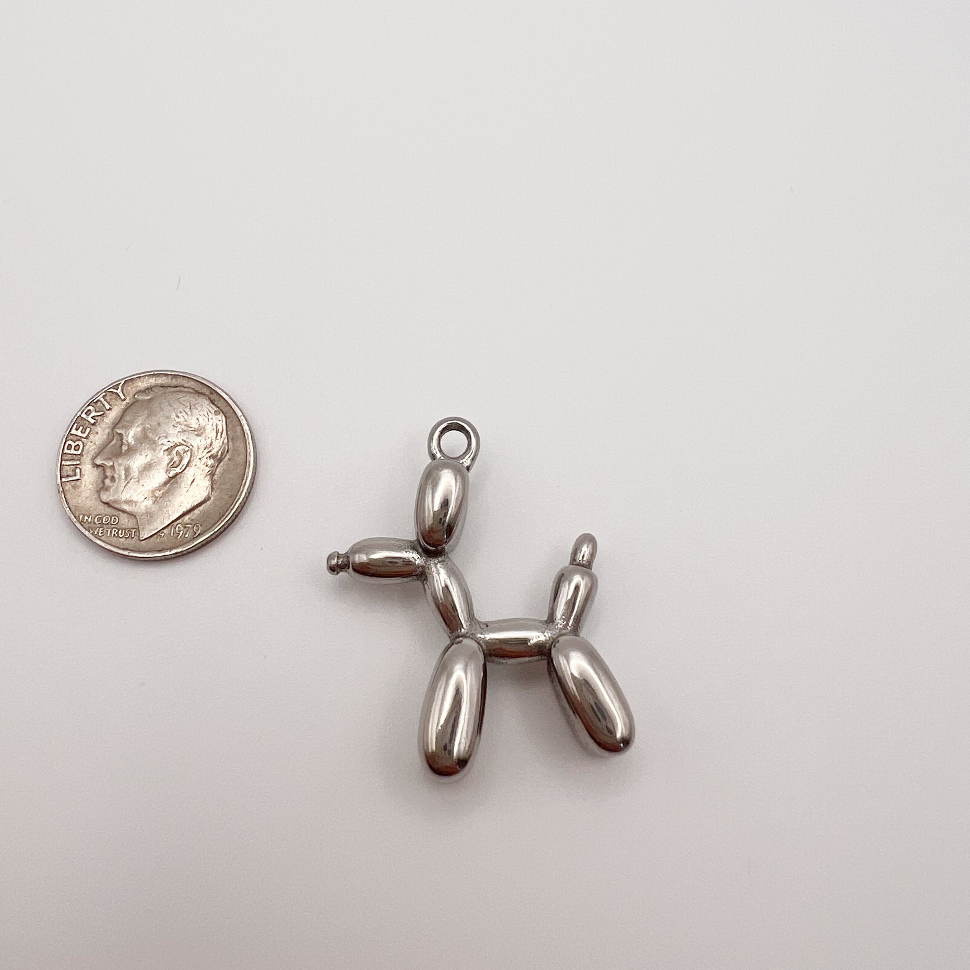 Metallic balloon dog charm next to a quarter on a white background