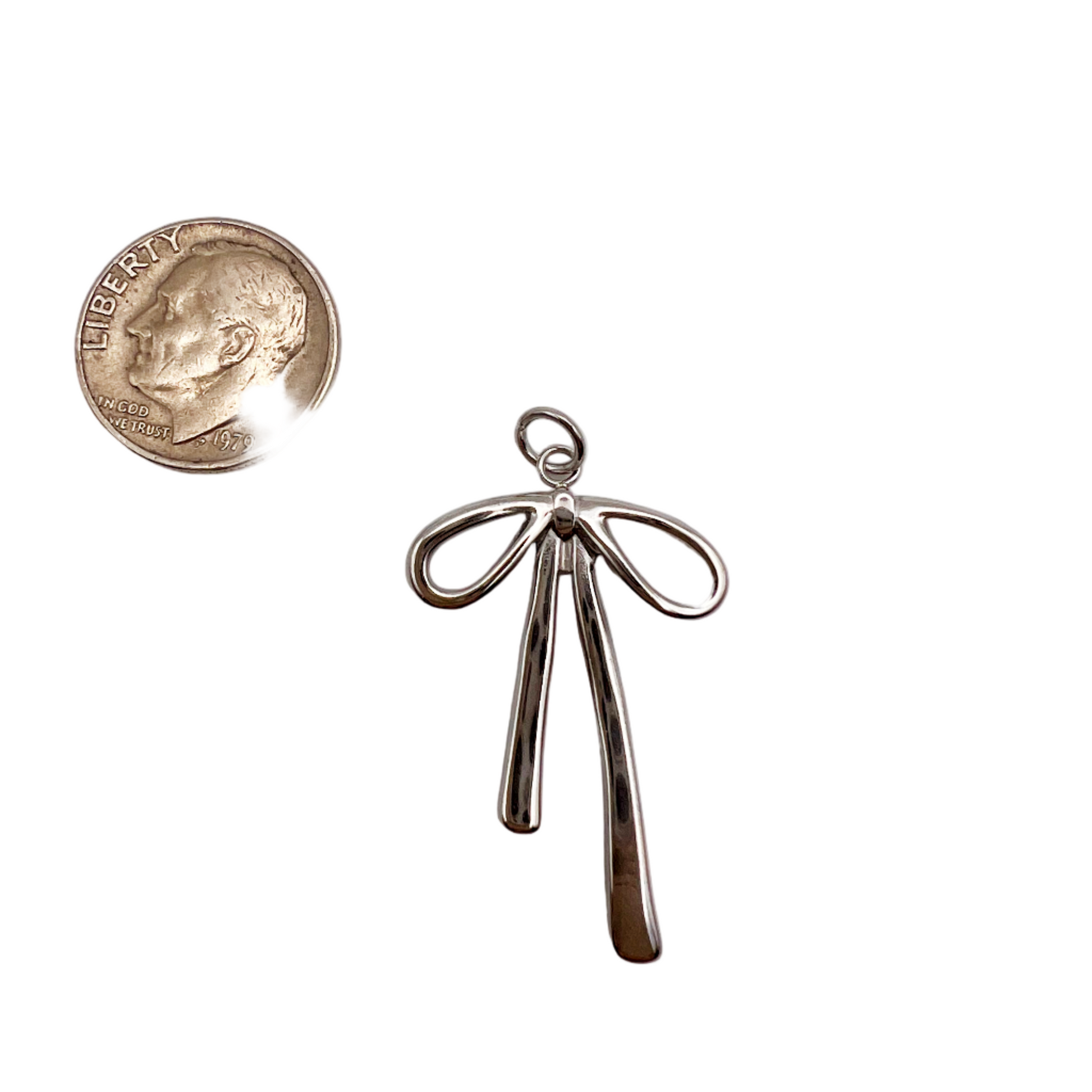 Silver bow-shaped pendant next to a quarter on a white background