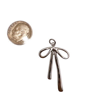 Silver bow-shaped pendant next to a quarter on a white background