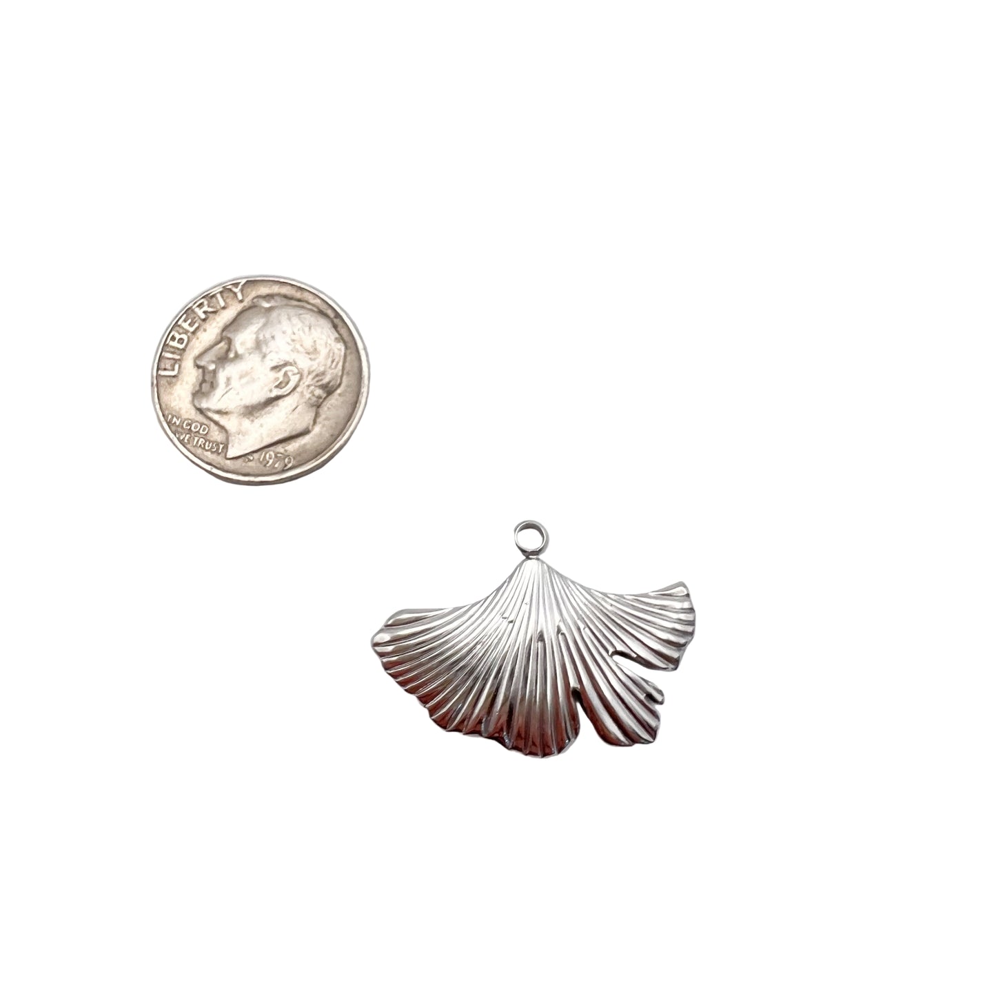 Silver shell pendant next to a quarter on a white background