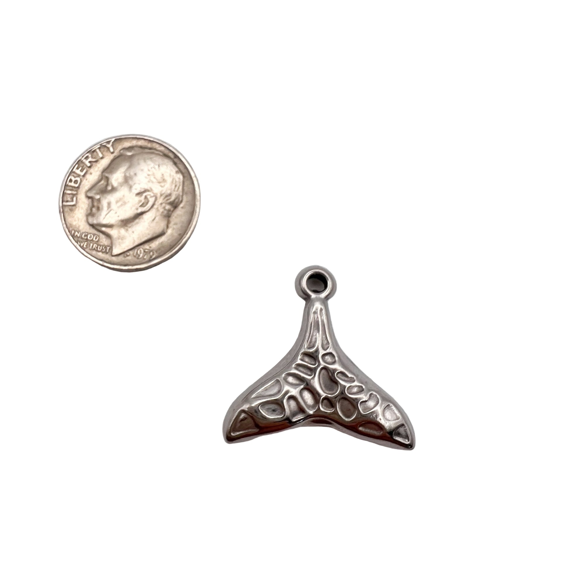 Silver whale tail pendant next to a quarter on a light gray background