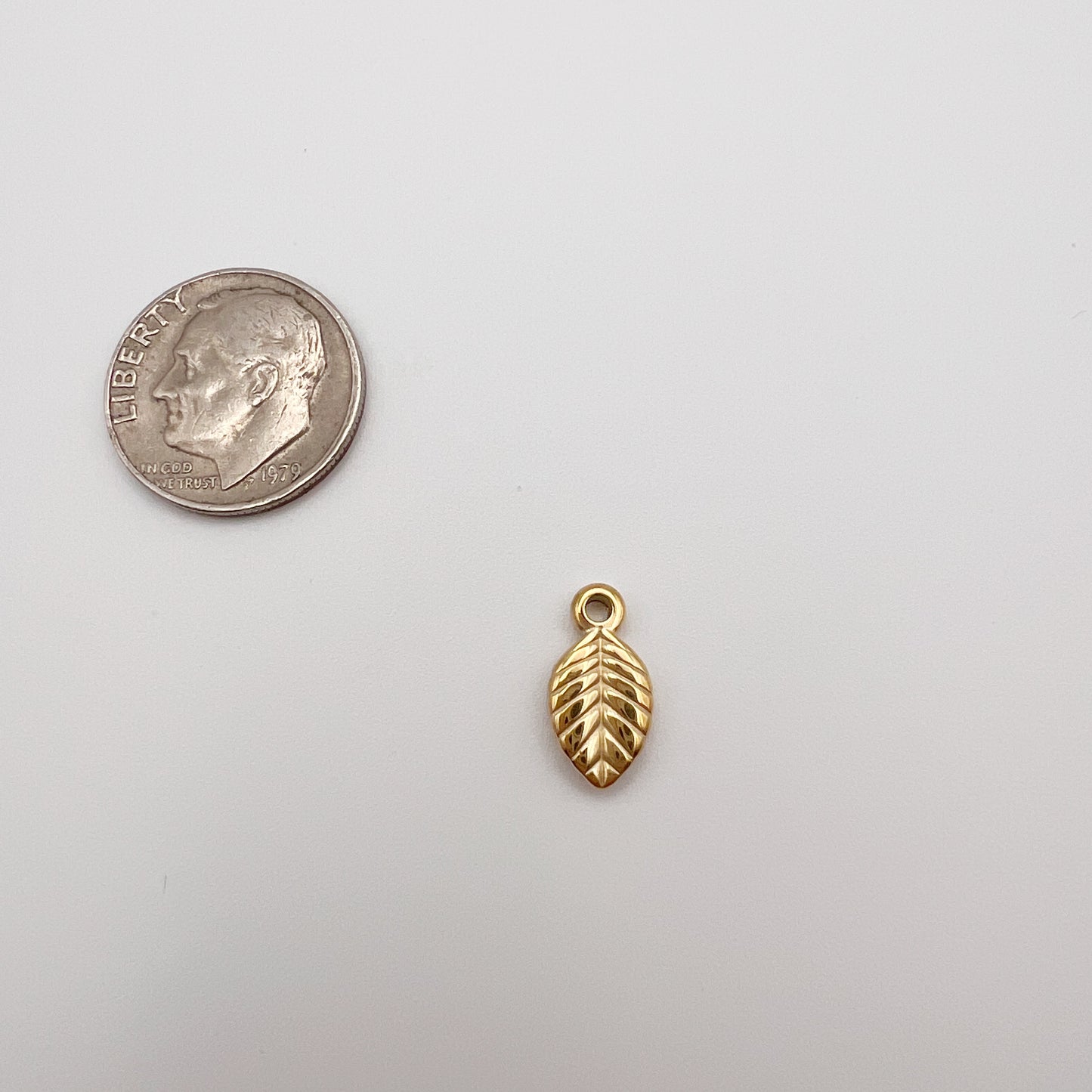 Gold leaf-shaped charm next to a quarter on a white background