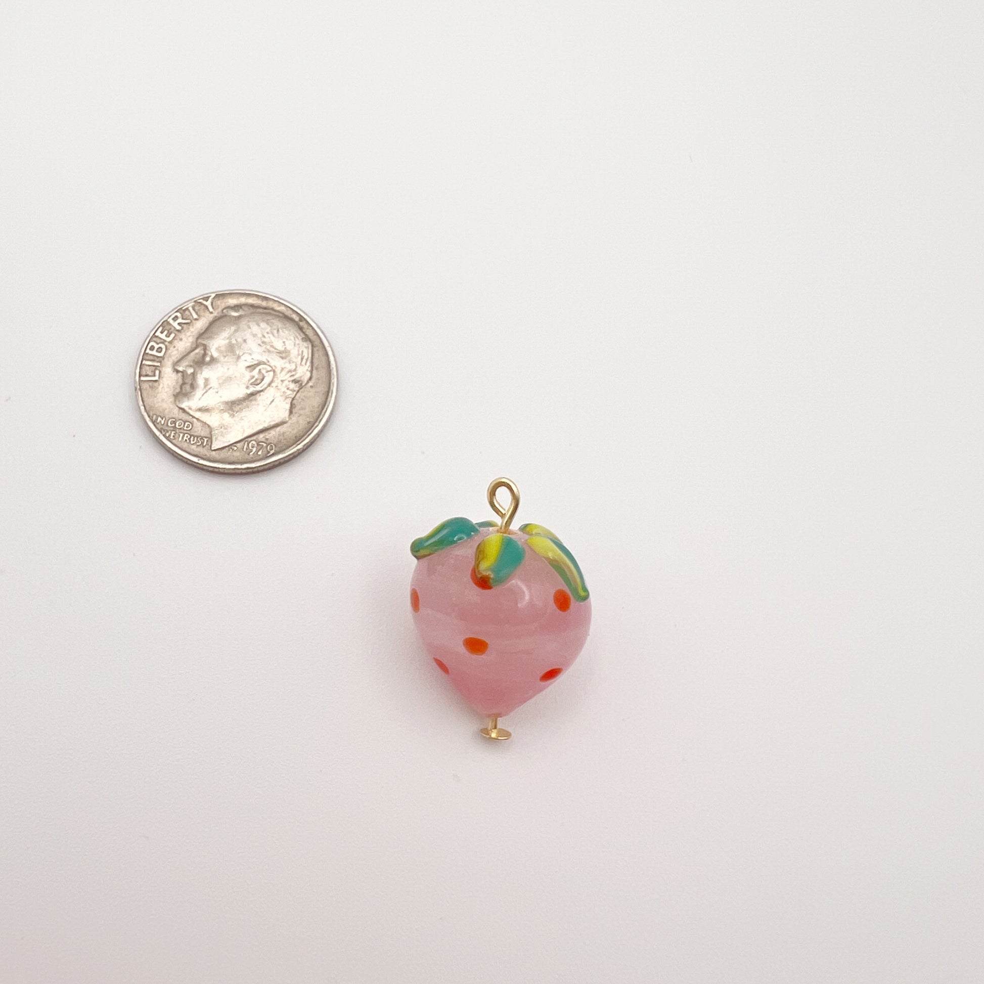 Small strawberry-shaped charm next to a quarter on a white background